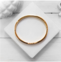 Load image into Gallery viewer, The Unity Bangle is modelled after the end of a bullet casing, featuring a similar groove and stamped markings around the front and back surfaces - a subtle, yet meaningful reference to Brass &amp; Unity’s story.   This bangle is 24K gold plated stainless steel with an integrated snap feature.    Size: SM/MD 
